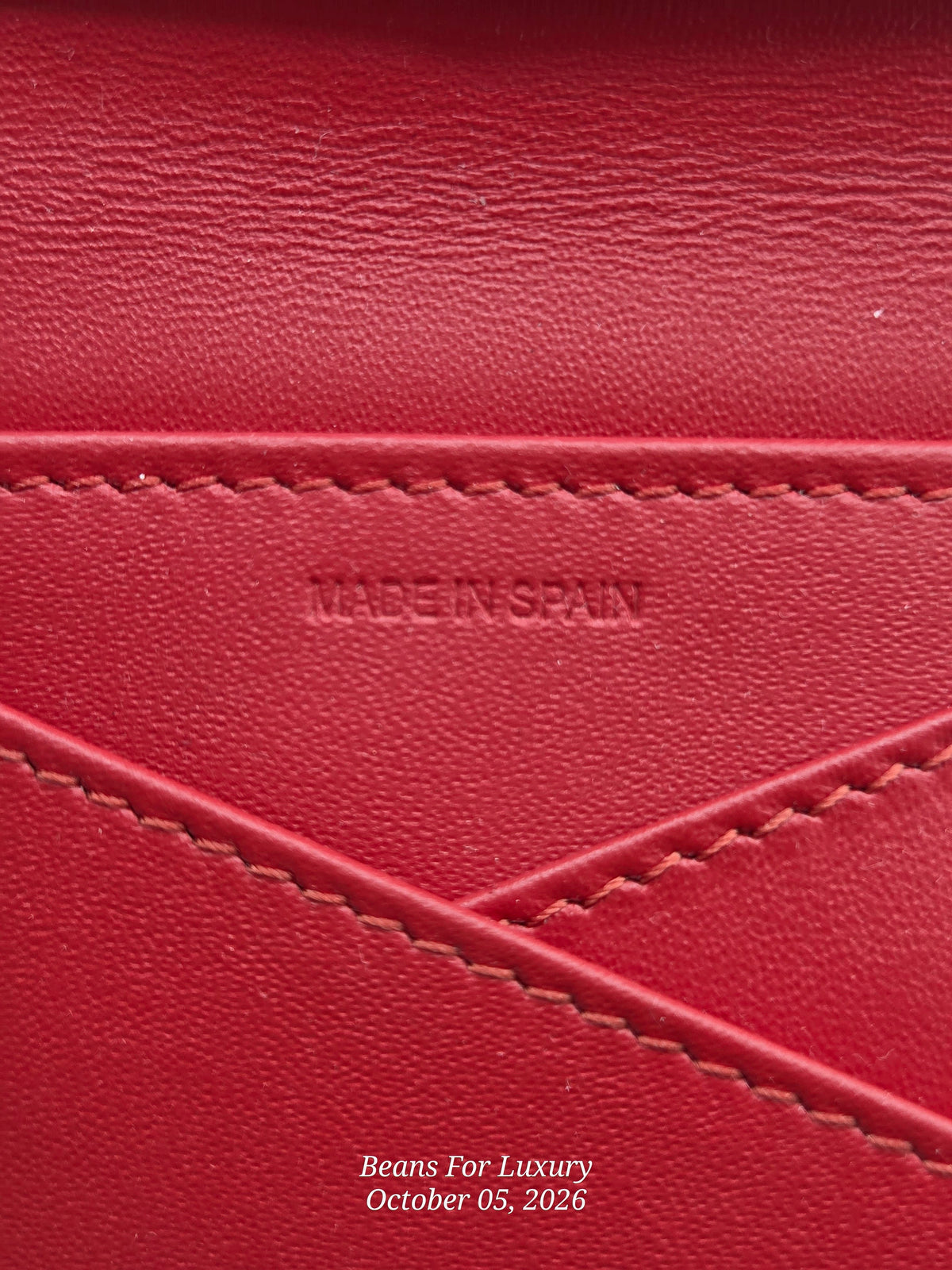 Close-up of a red leather surface with visible stitching and an embossed 'MADE IN SPAIN' mark, plus a small 'Beans For Luxury' watermark near the bottom.