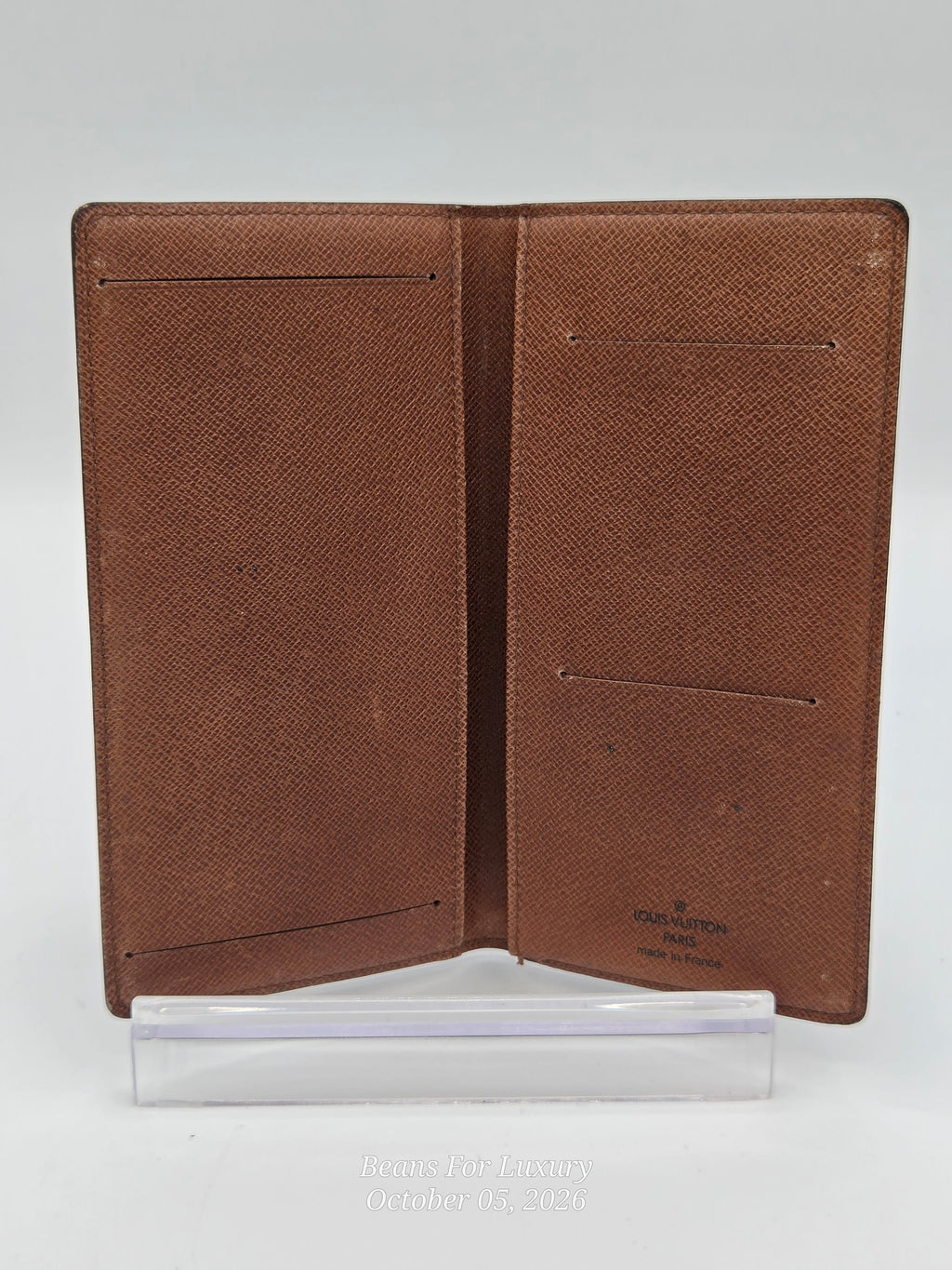 A brown textured leather passport cover shown open, displaying multiple interior card slots and pockets, standing on a clear plastic display block against a light gray background.