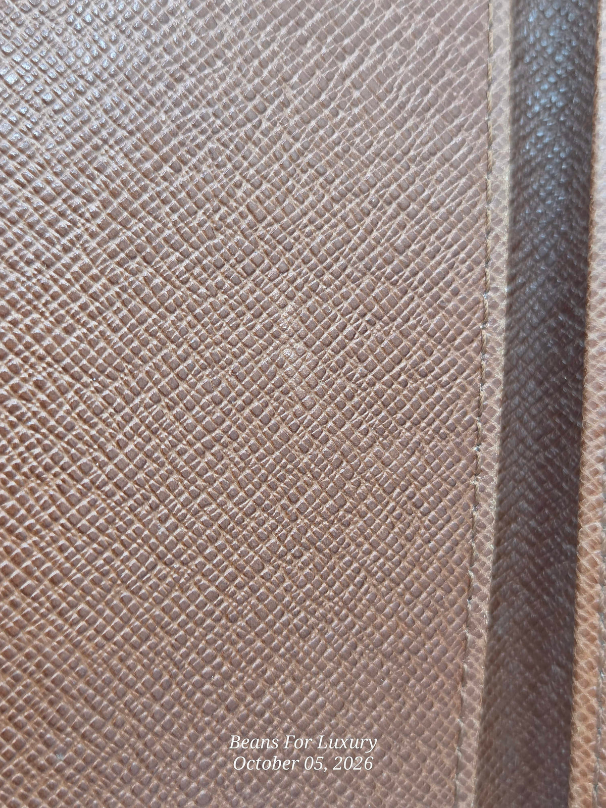 Close-up of a textured fabric material in a warm taupe-brown color, showing a fine woven pattern and a vertical seam on the right side.
