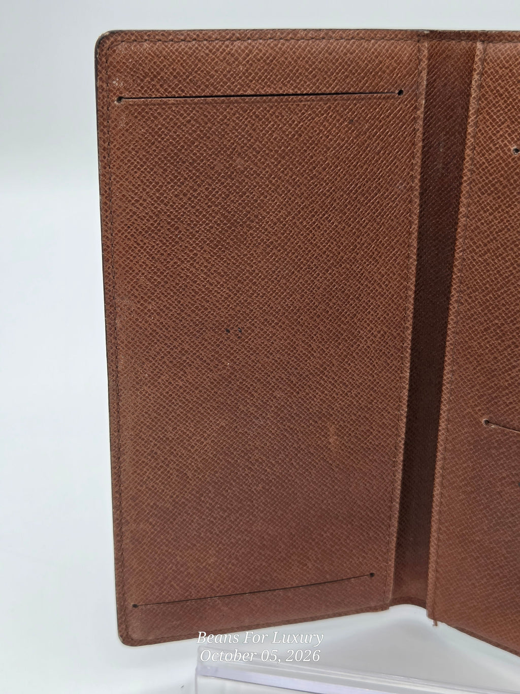 A close-up of a brown textured leather wallet or passport cover, showing the interior card slots and stitched edges against a white background.