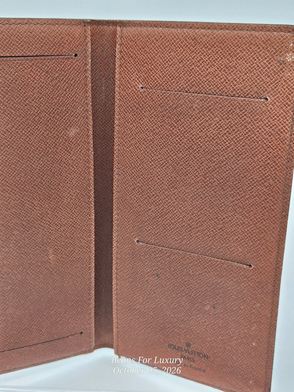 An open brown textured leather passport cover or wallet with multiple interior pockets, photographed against a light background. A small 'COEUR D'ARMES' logo is visible near the bottom right, and a watermark reading 'Moms For Luxury October 25, 2026' appears at the bottom.