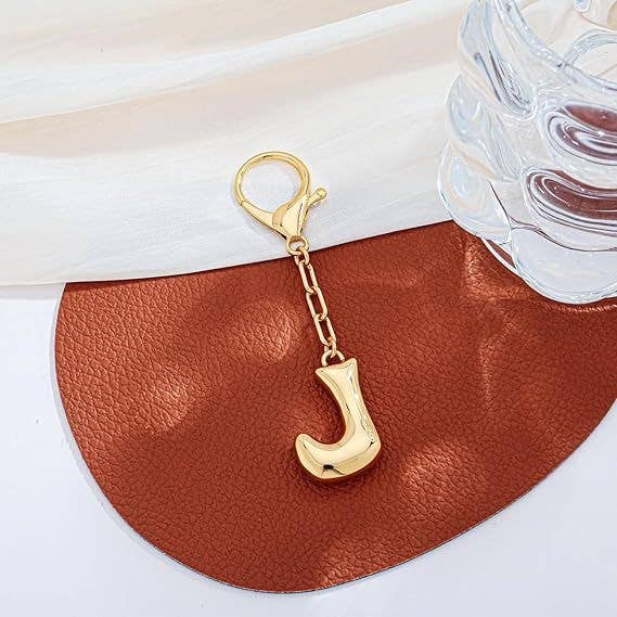 Gold keychain with letter 'J' on a brown leather surface