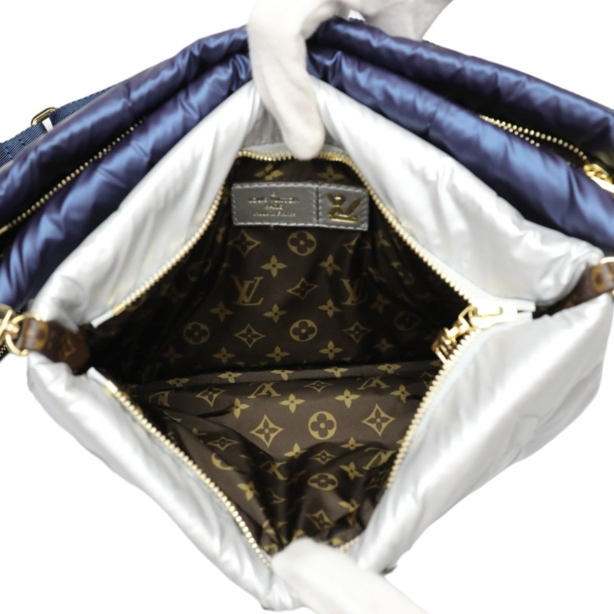 Designer handbag with monogram pattern interior, held open by a white glove.
