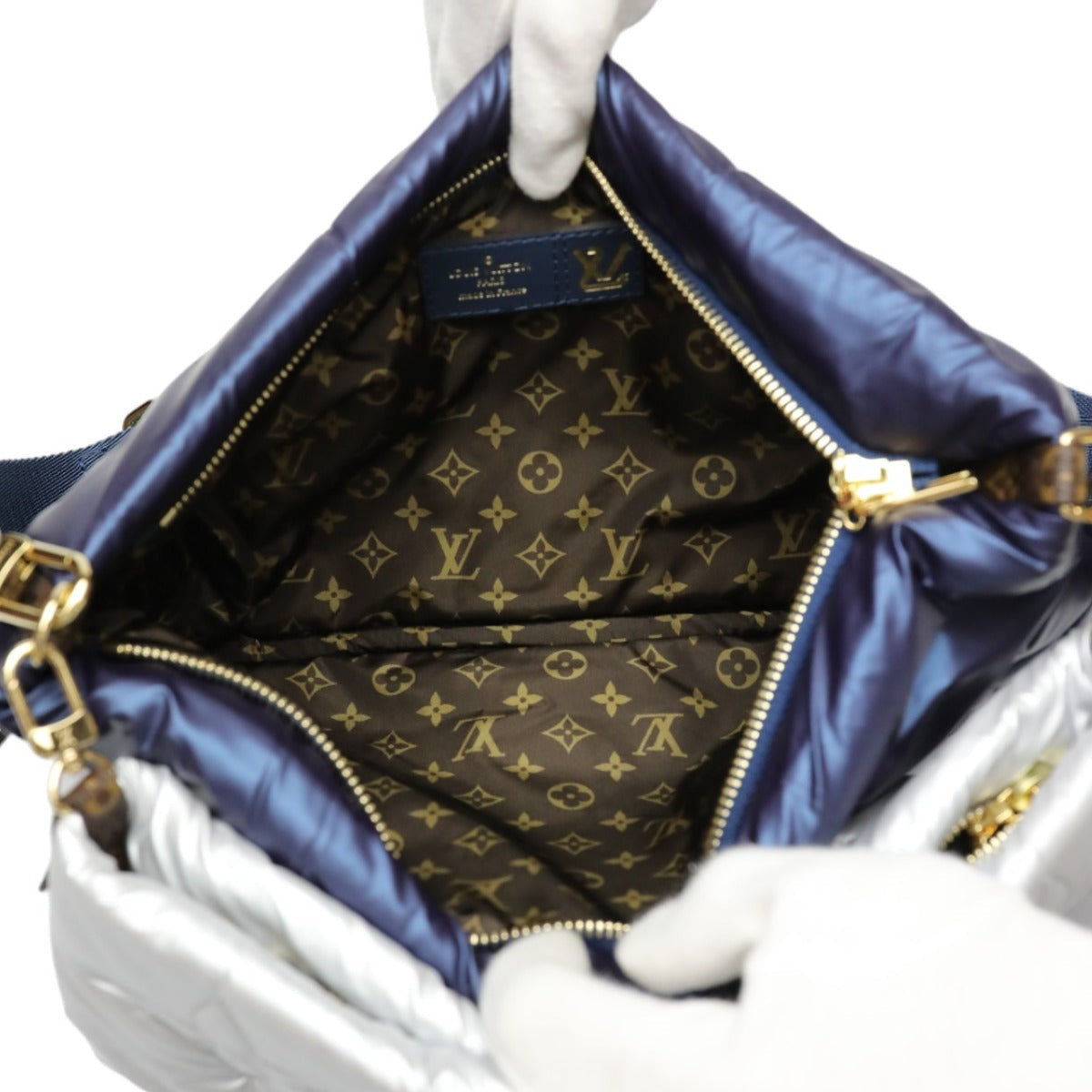 Louis Vuitton handbag with monogram pattern and blue interior, held by white-gloved hands.