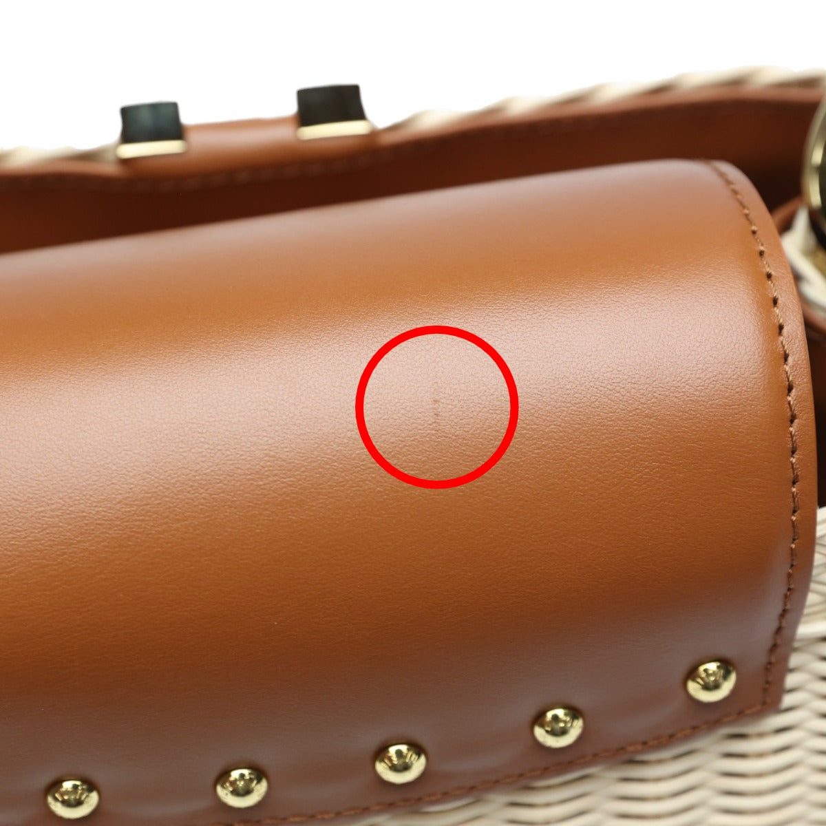 Brown leather handbag with gold studs and a red circle highlighting a spot on the surface.