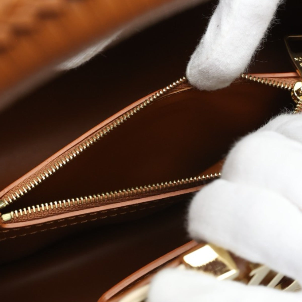 Close-up of a brown leather handbag with gold zipper, held by white rabbit paws.