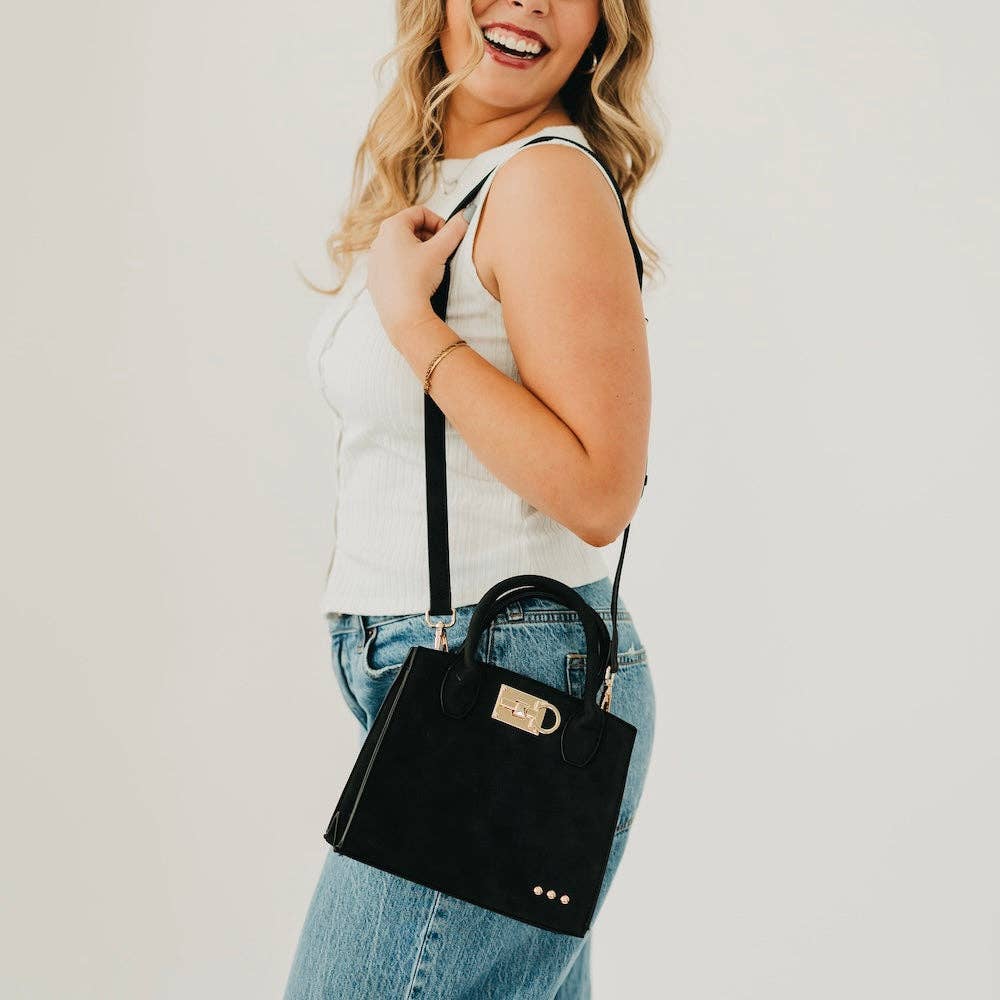 Woman holding a black handbag against a plain background
