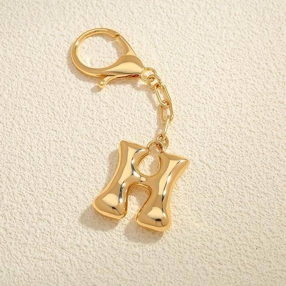 Gold keychain with letter 'H' on a beige background