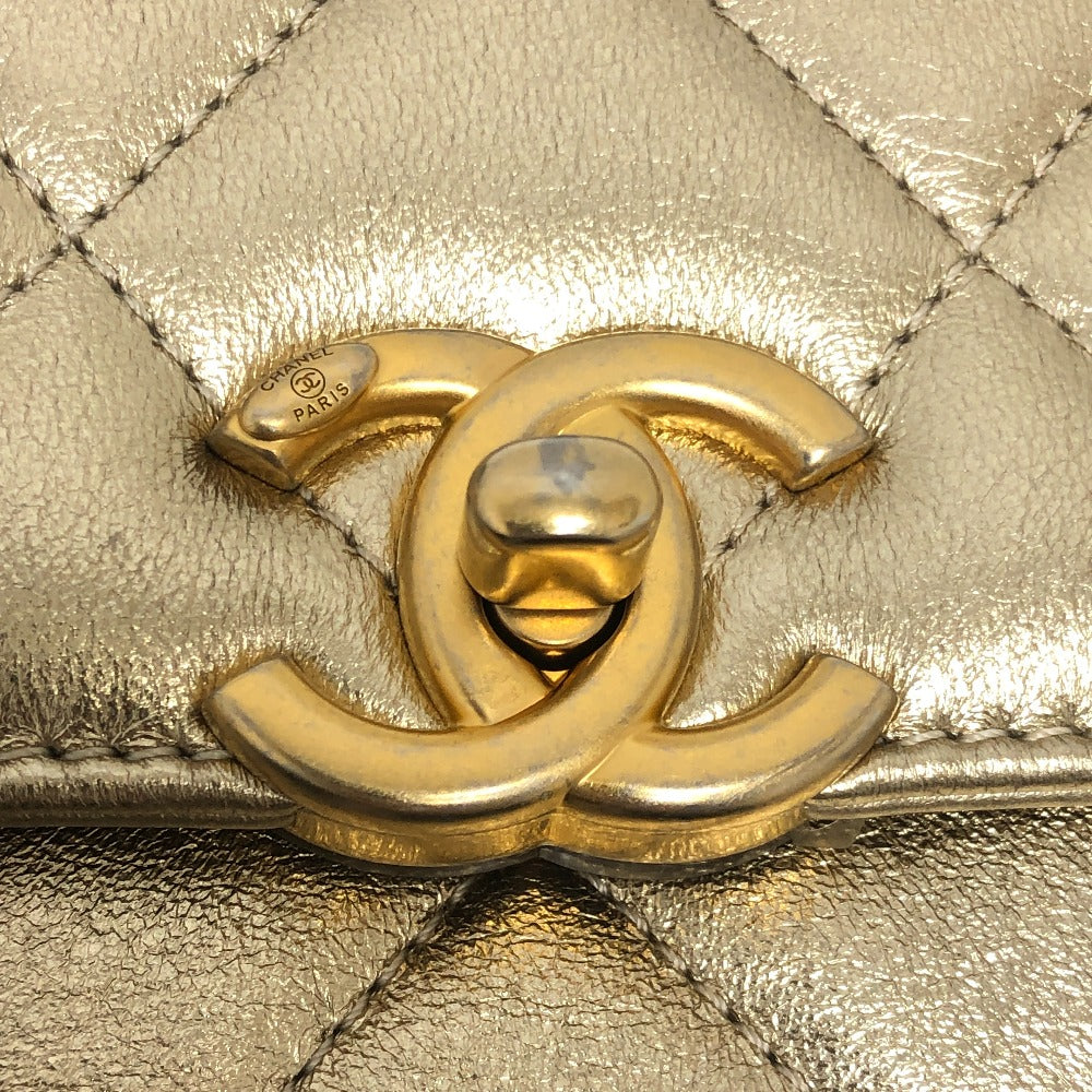 Close-up of a gold Chanel logo on a quilted handbag.
