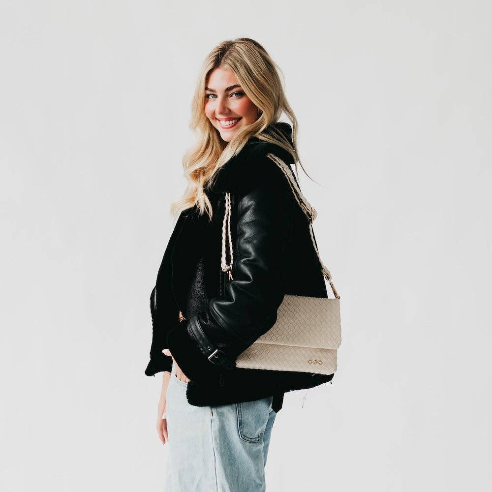 Woman wearing a black leather jacket holding a beige tote bag against a white background