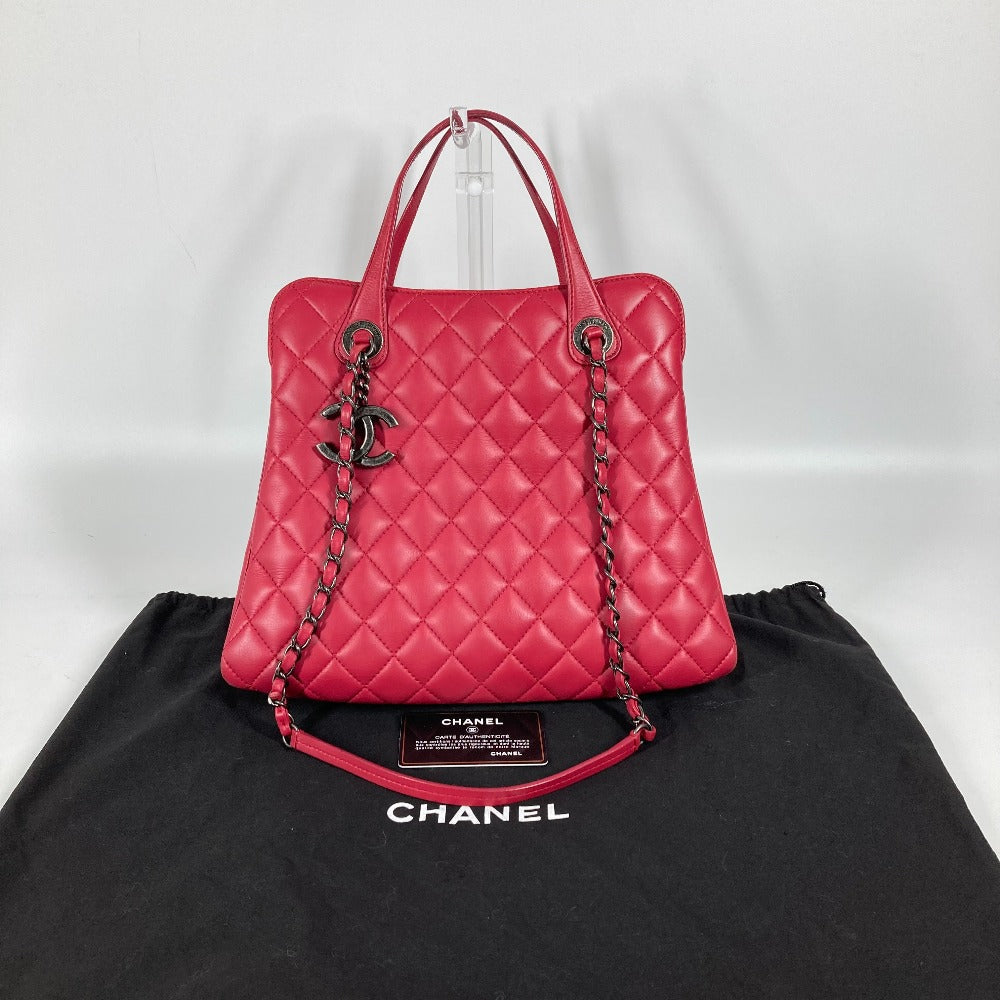 Pink quilted handbag with chain detail on a black Chanel garment against a white background