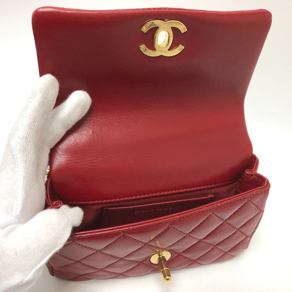Red quilted handbag with gold CC logo held by a gloved hand on a white background