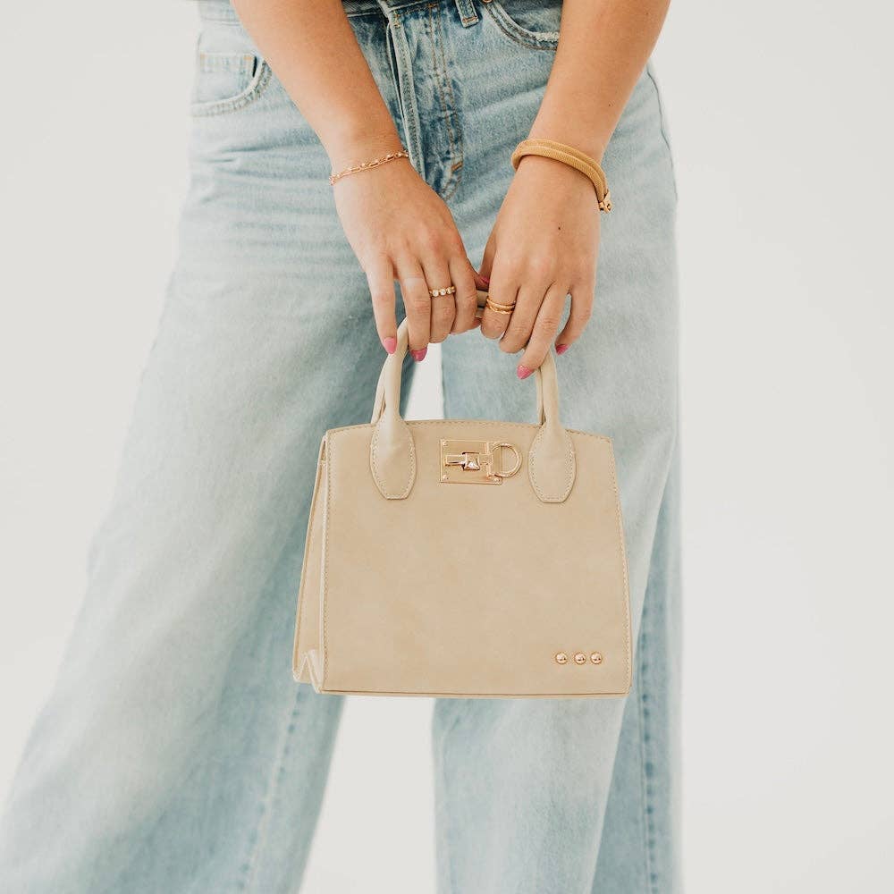 Beige handbag held by a person wearing light blue jeans on a neutral background