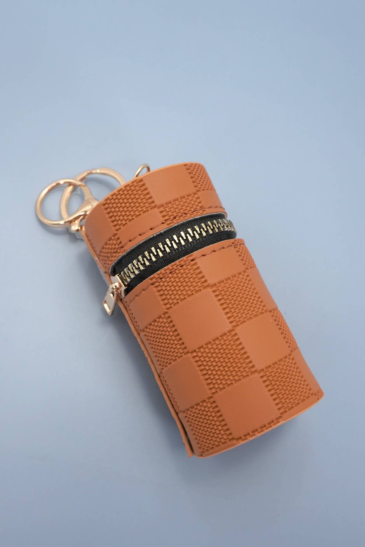 Brown textured keychain pouch with gold ring on a light blue background