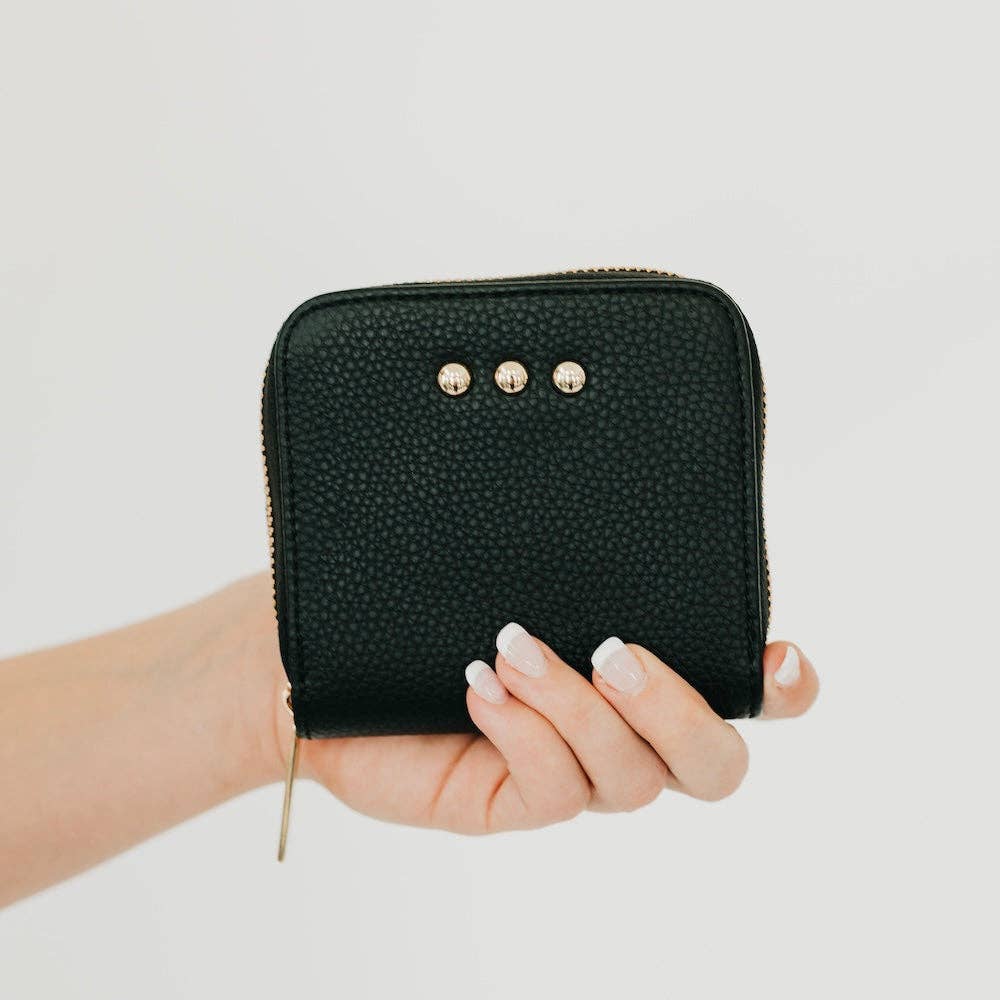 Hand holding a black textured wallet with gold accents on a light gray background