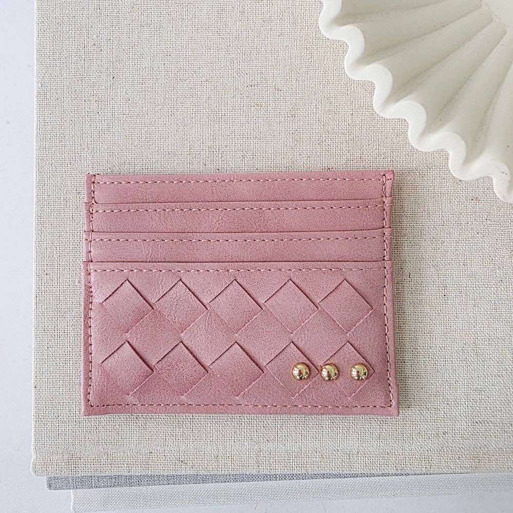 Pink woven cardholder with gold studs on a textured beige surface