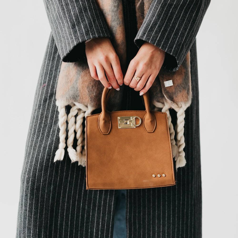 Person holding a brown leather handbag with a plain background