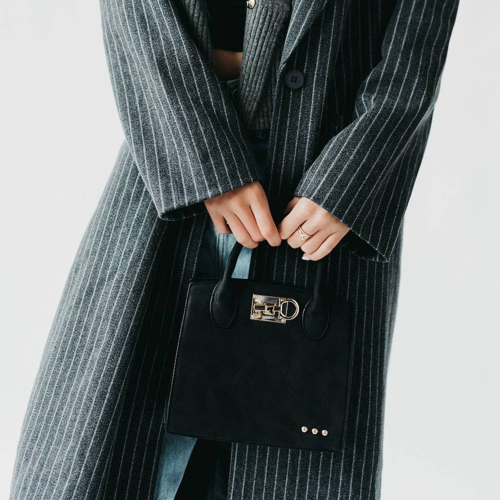 Person wearing a long pinstripe coat holding a black handbag with a gold clasp.
