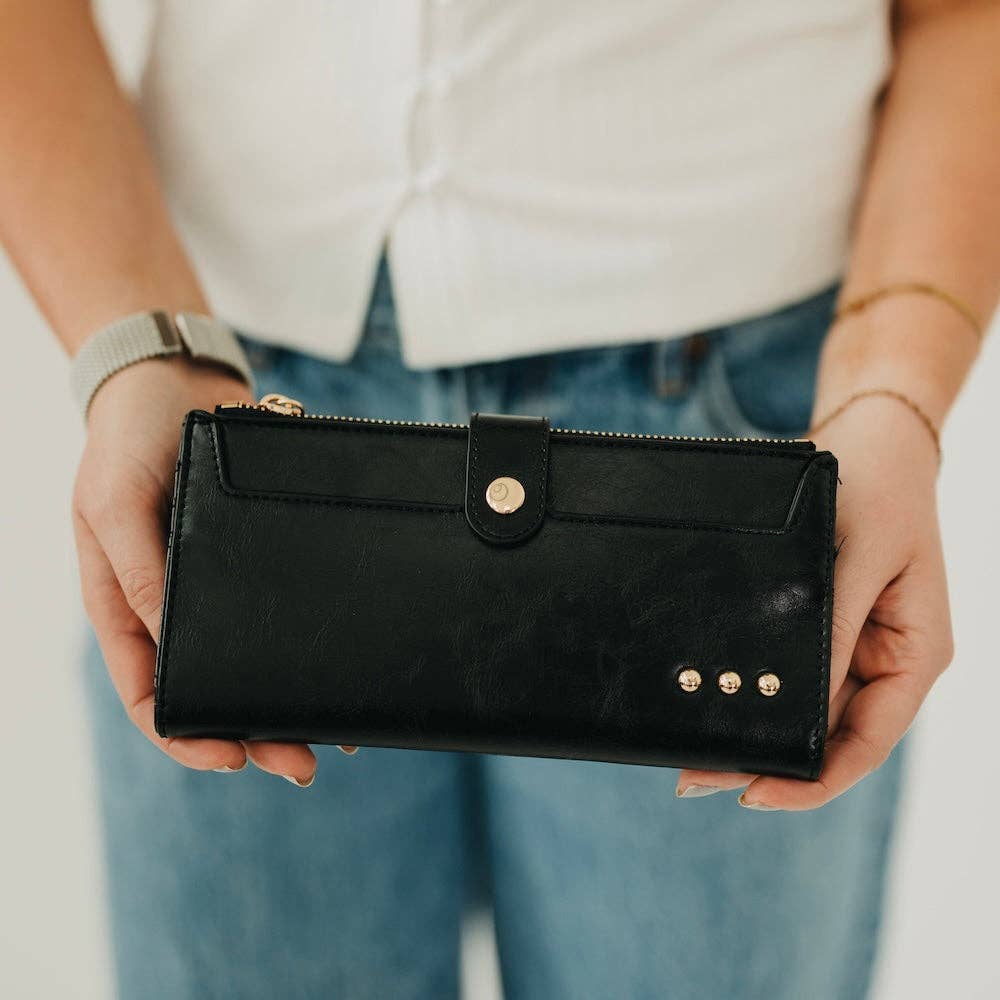 Person holding a black wallet with gold studs against a neutral background