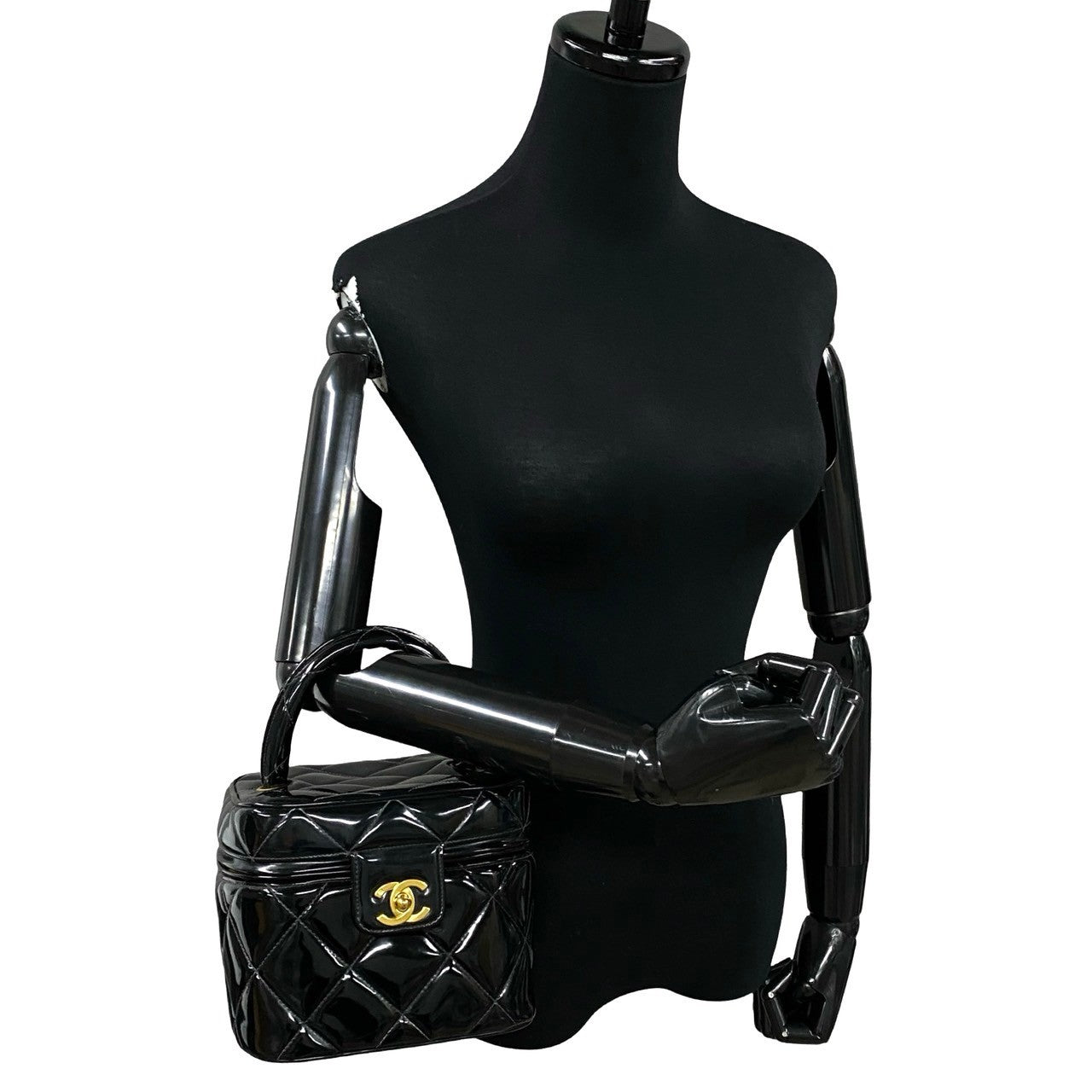 Black quilted handbag with gold clasp on a black mannequin against a white background