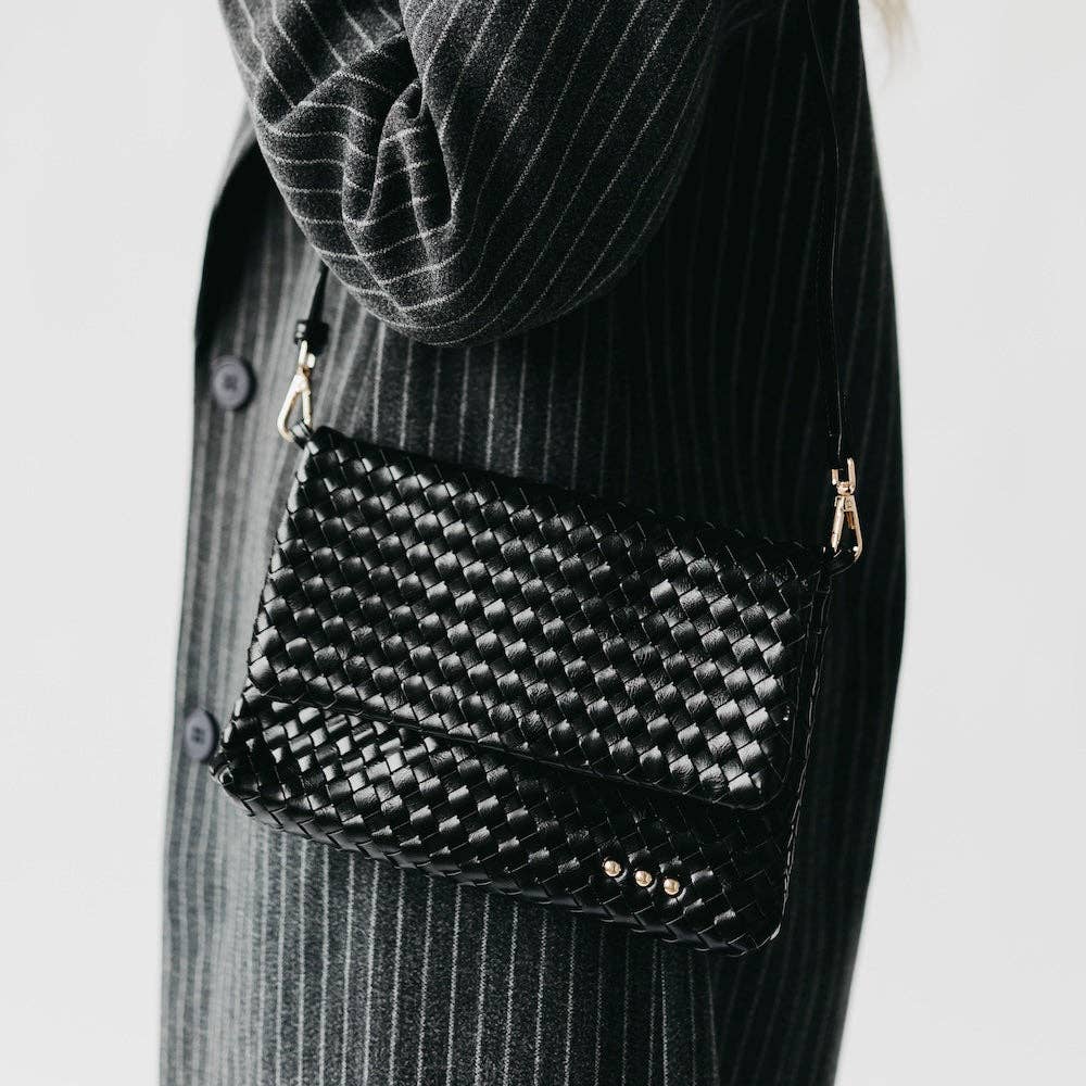 Black woven handbag with gold accents worn over a person's shoulder against a neutral background