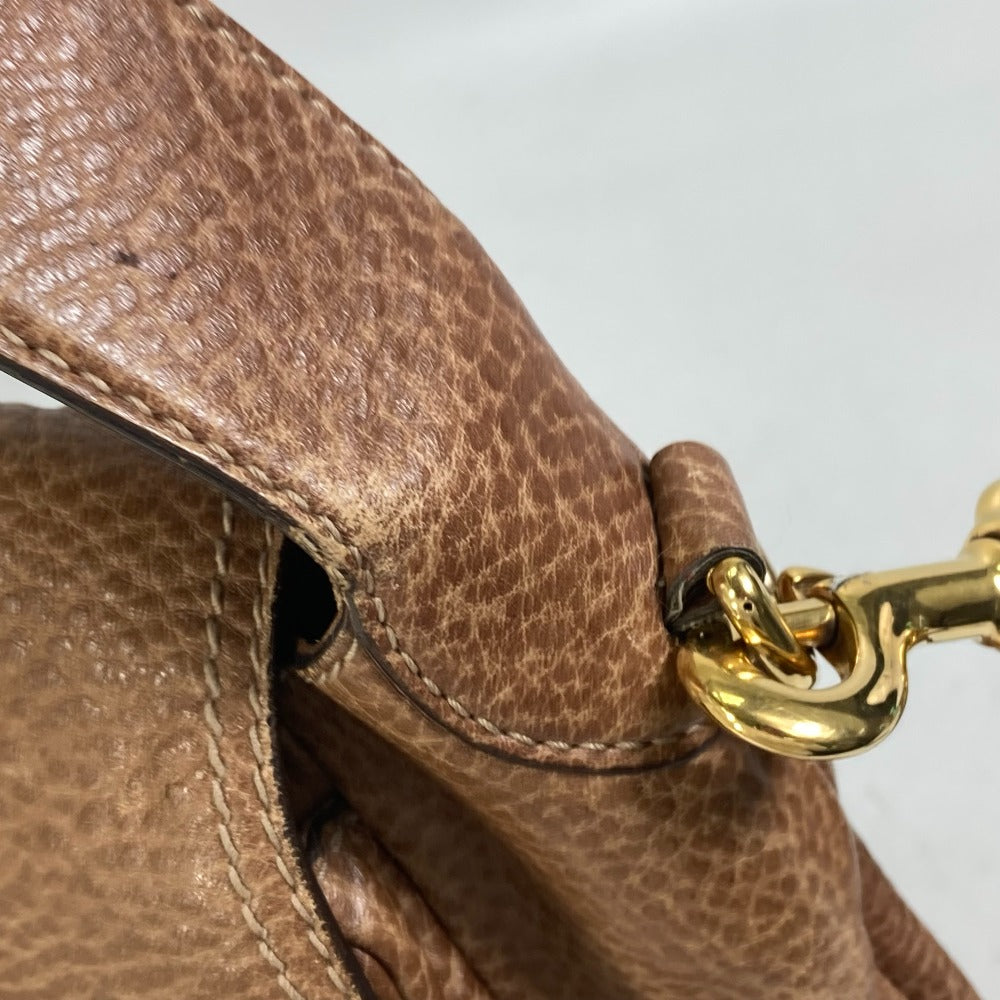 Close-up of a brown leather handbag with a gold metal clasp on a light gray background