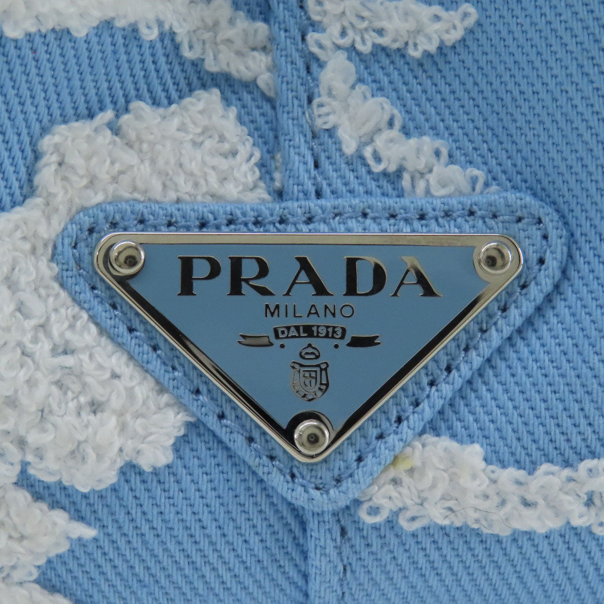Close-up of a Prada logo on a blue fabric background with lace details