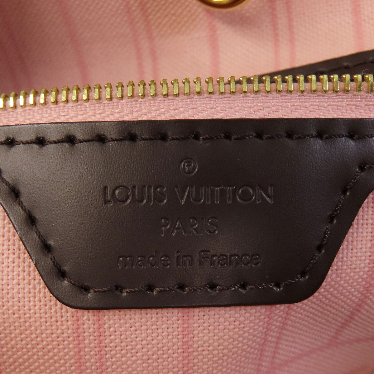 Louis Vuitton bag with gold zipper and visible branding on a pink plaid background