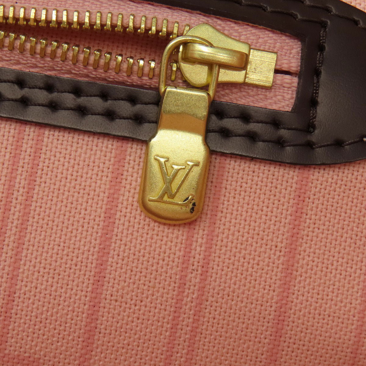 Close-up of a gold zipper pull on a pink textured surface with a brand logo.