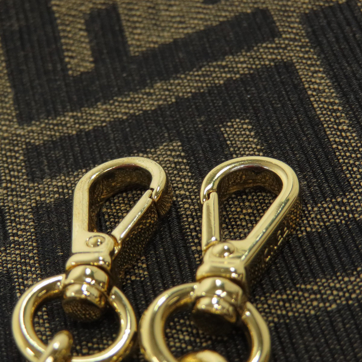 Two gold metal hooks on a textured brown fabric background