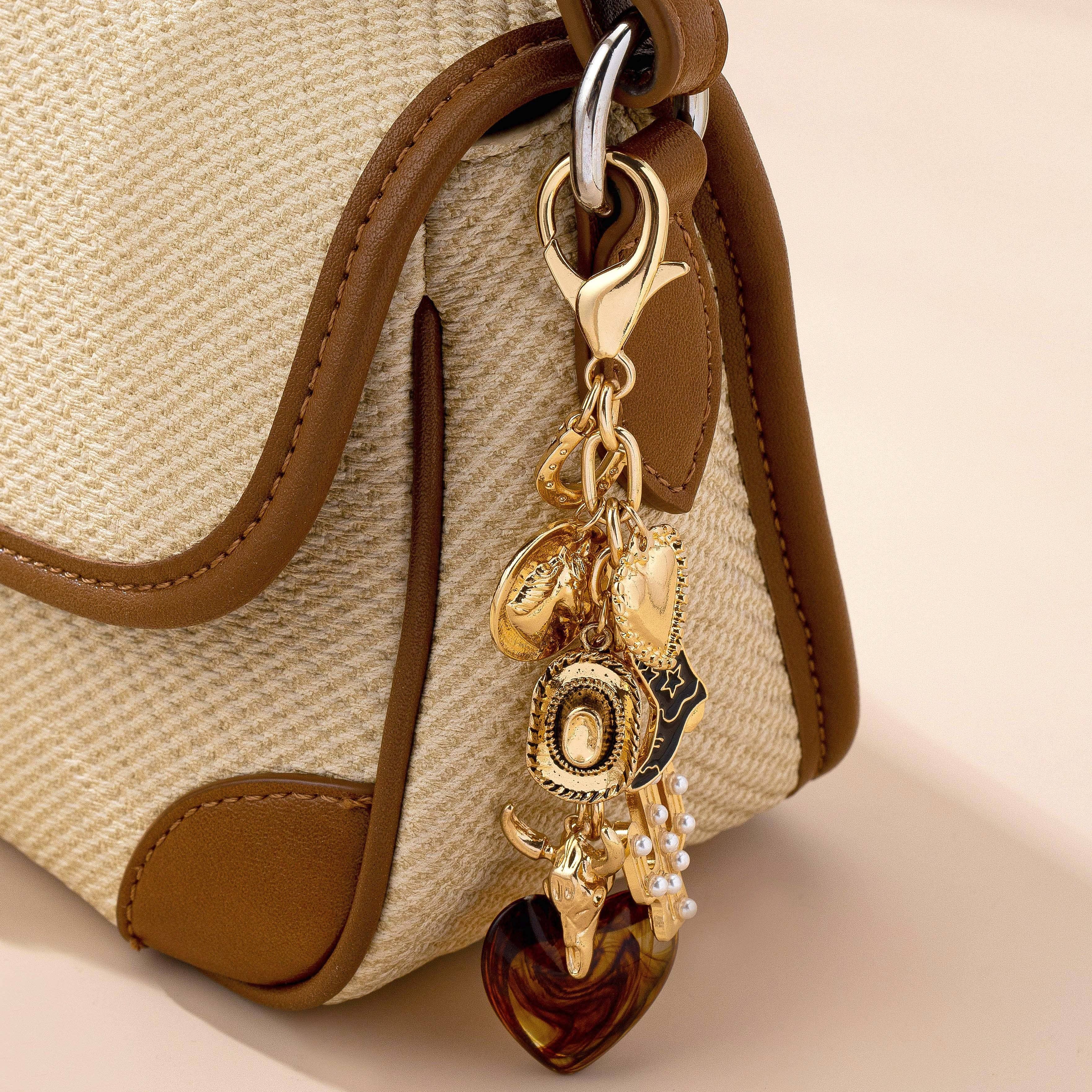 Gold charm keychain attached to a beige handbag with brown handles.