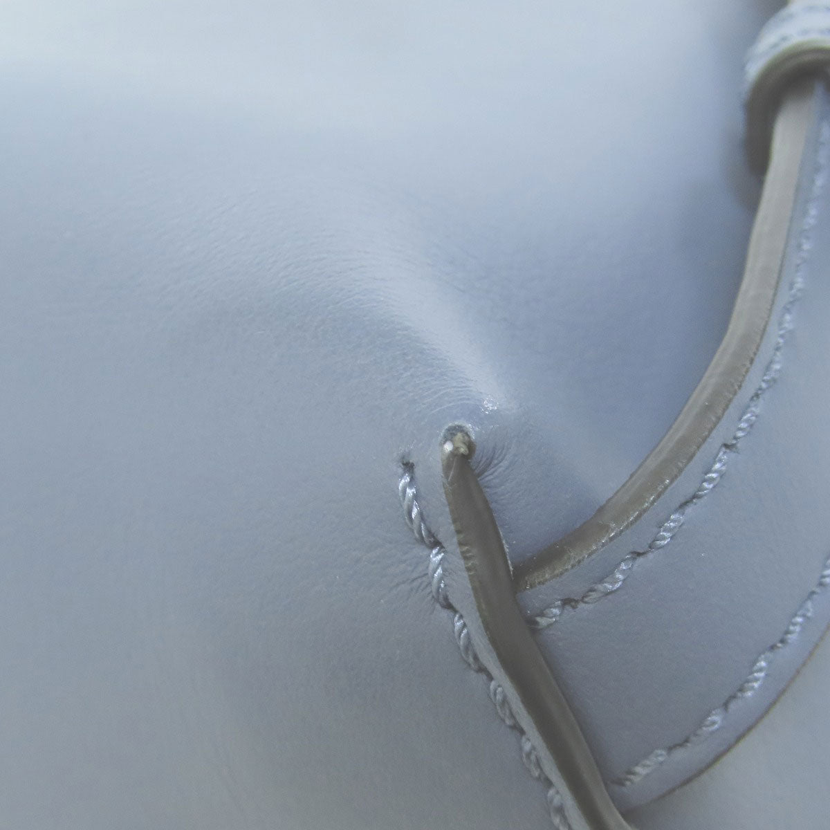 Close-up of a white leather product with stitching detail on a light gray background