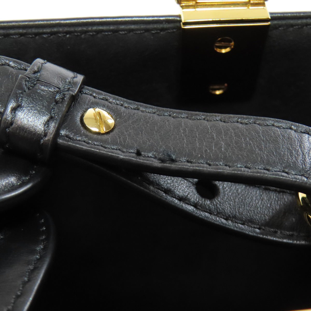 Close-up of a black leather handbag handle with gold hardware on a dark background