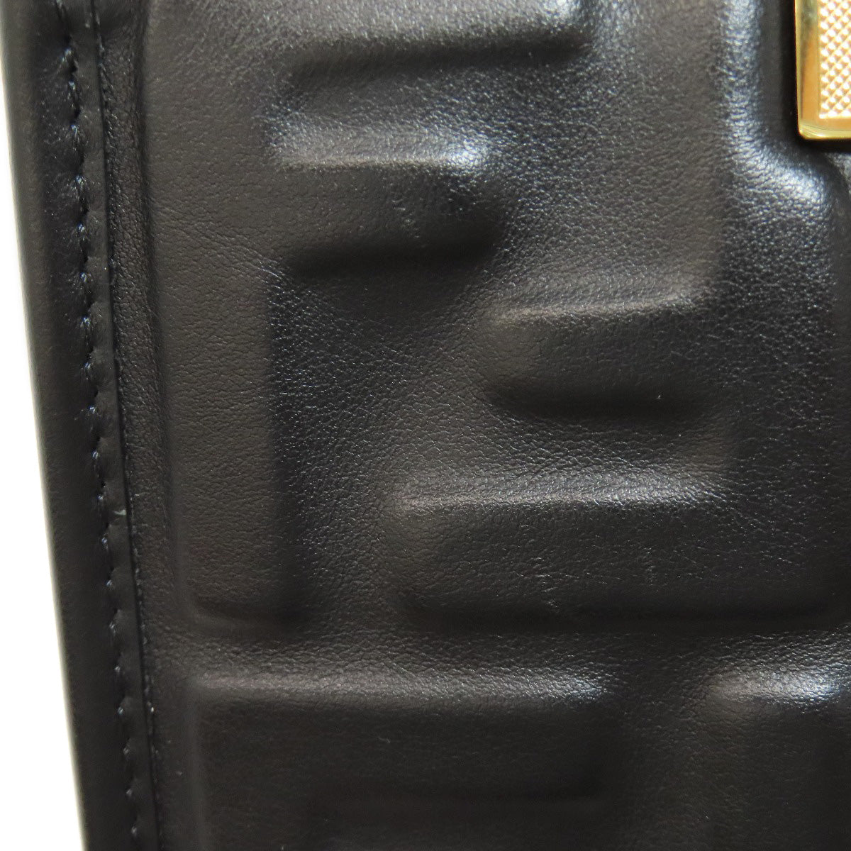 Close-up of a black textured leather product with a gold accent.