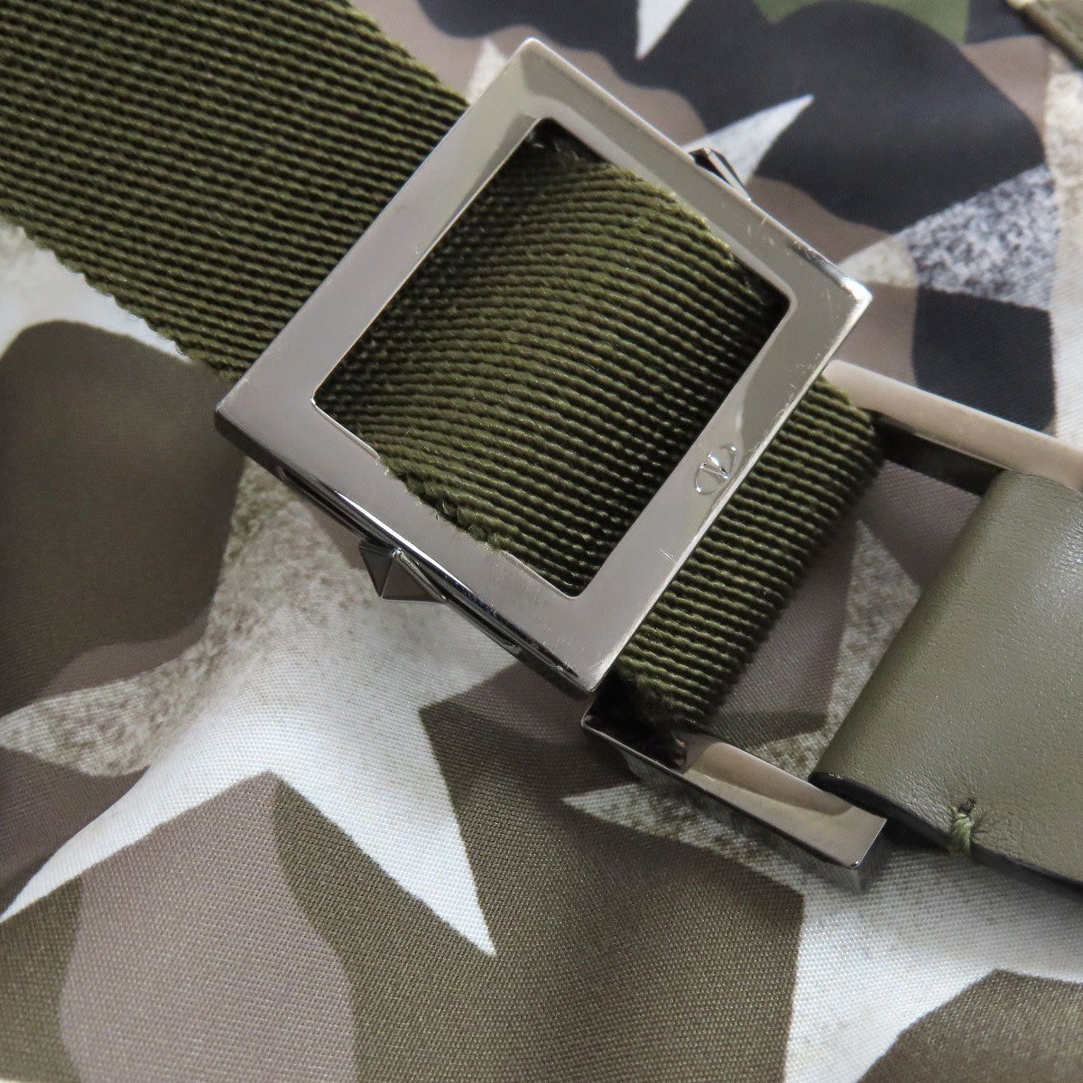 Green belt with a silver buckle on a camouflage-patterned surface
