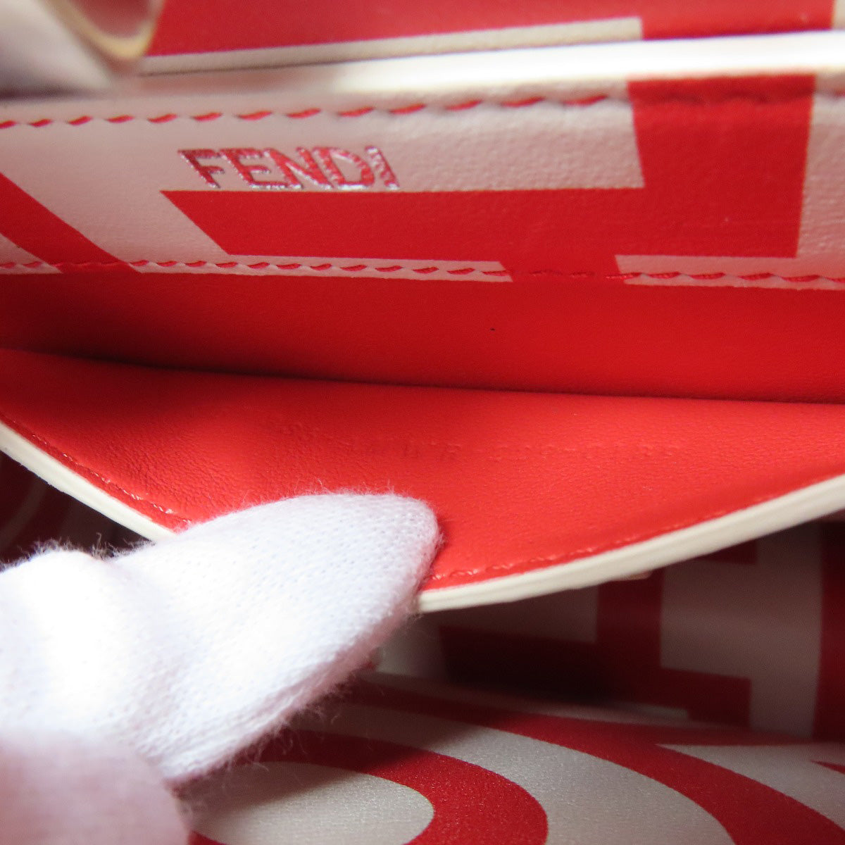 Close-up of a red and white Fendi handbag with a gloved hand holding it.