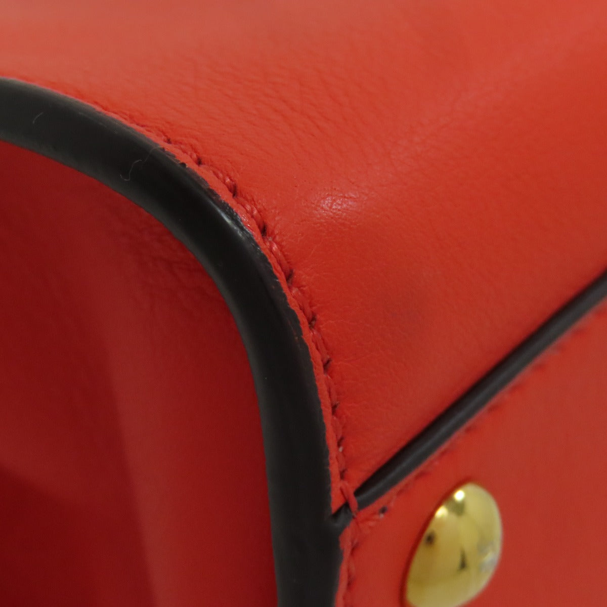 Close-up of a red leather product with a gold button and black trim.