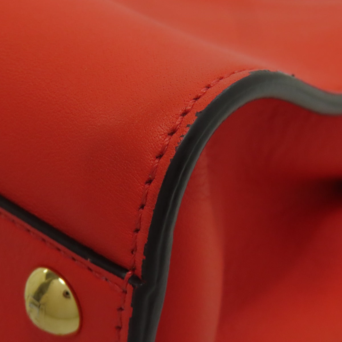 Close-up of a red leather product with a gold button detail