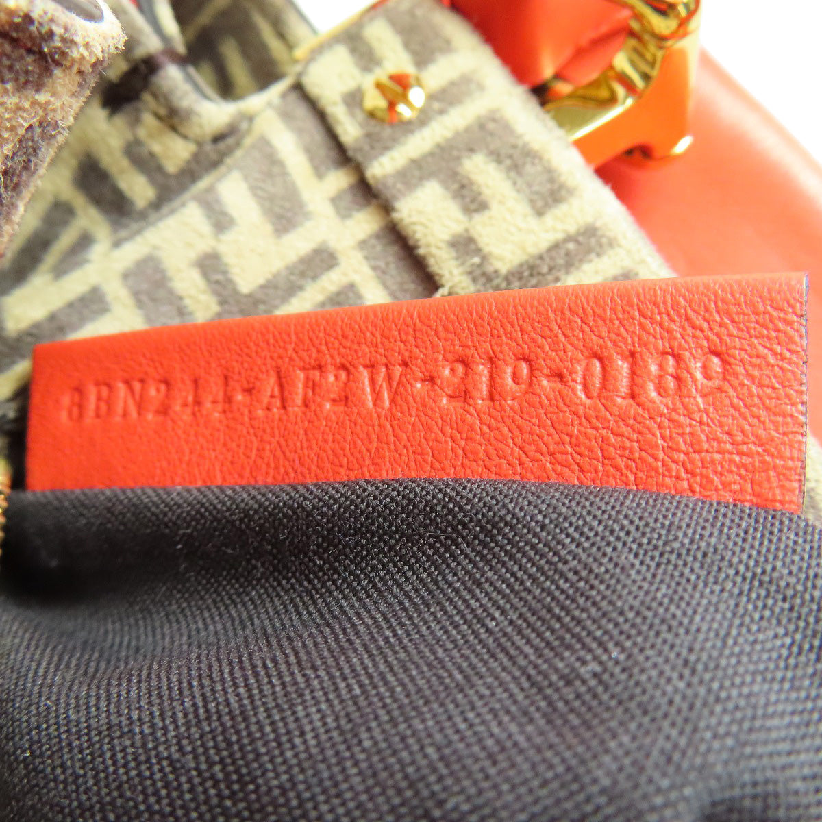 Close-up of a textured red tag on a black and orange bag with visible branding.