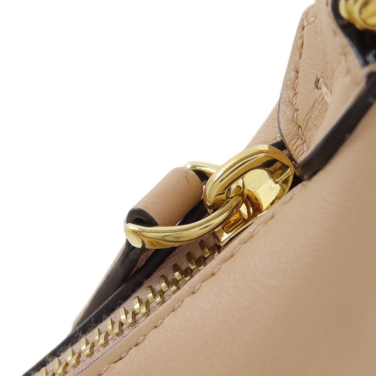 Close-up of a beige handbag with a gold zipper pull on a white background