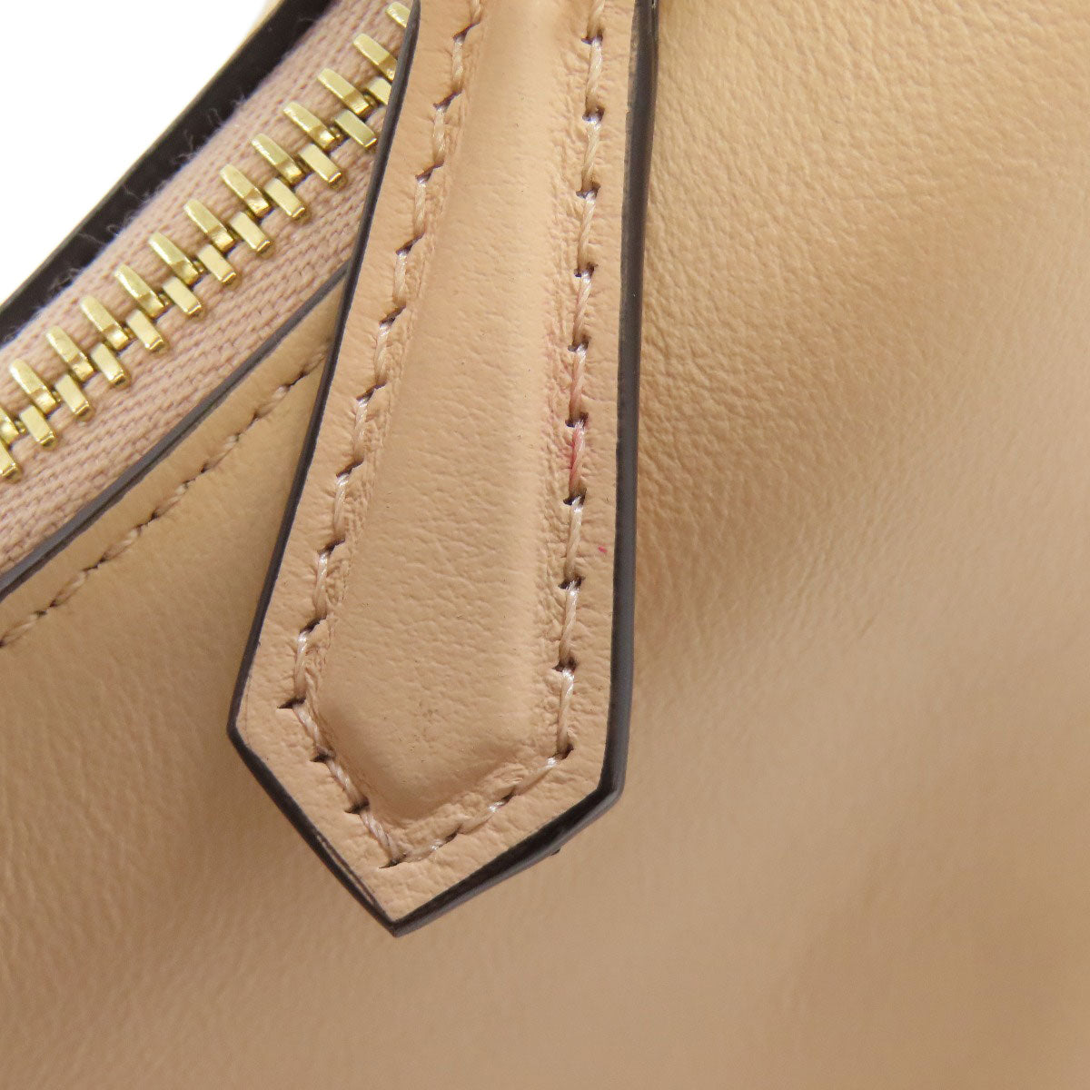 Close-up of a beige leather bag with gold zipper and stitching details.