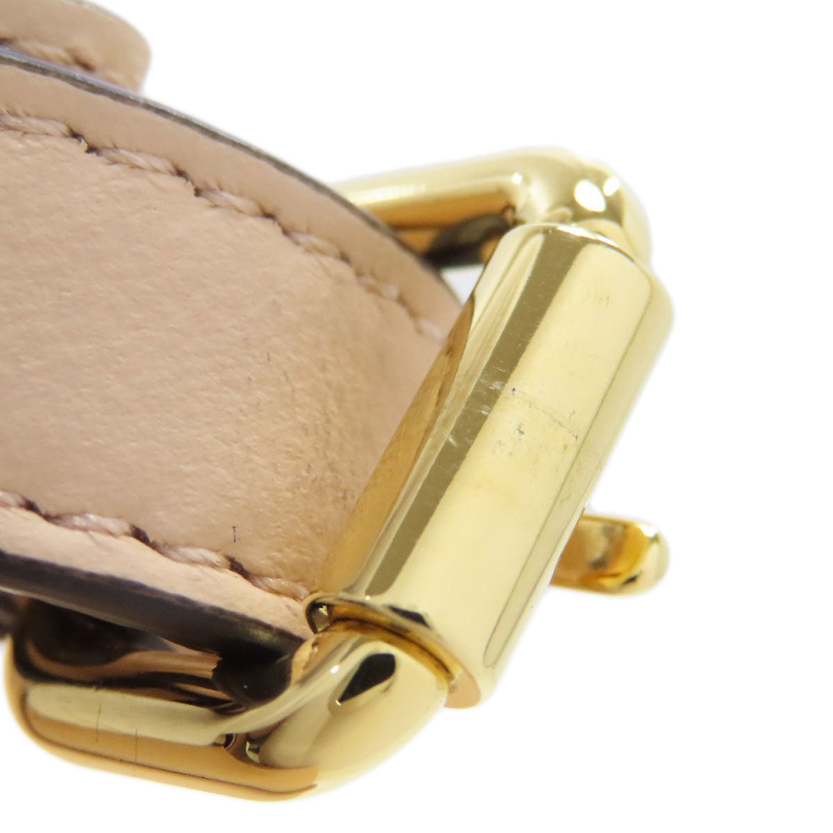Close-up of a gold buckle on beige leather, with a white background