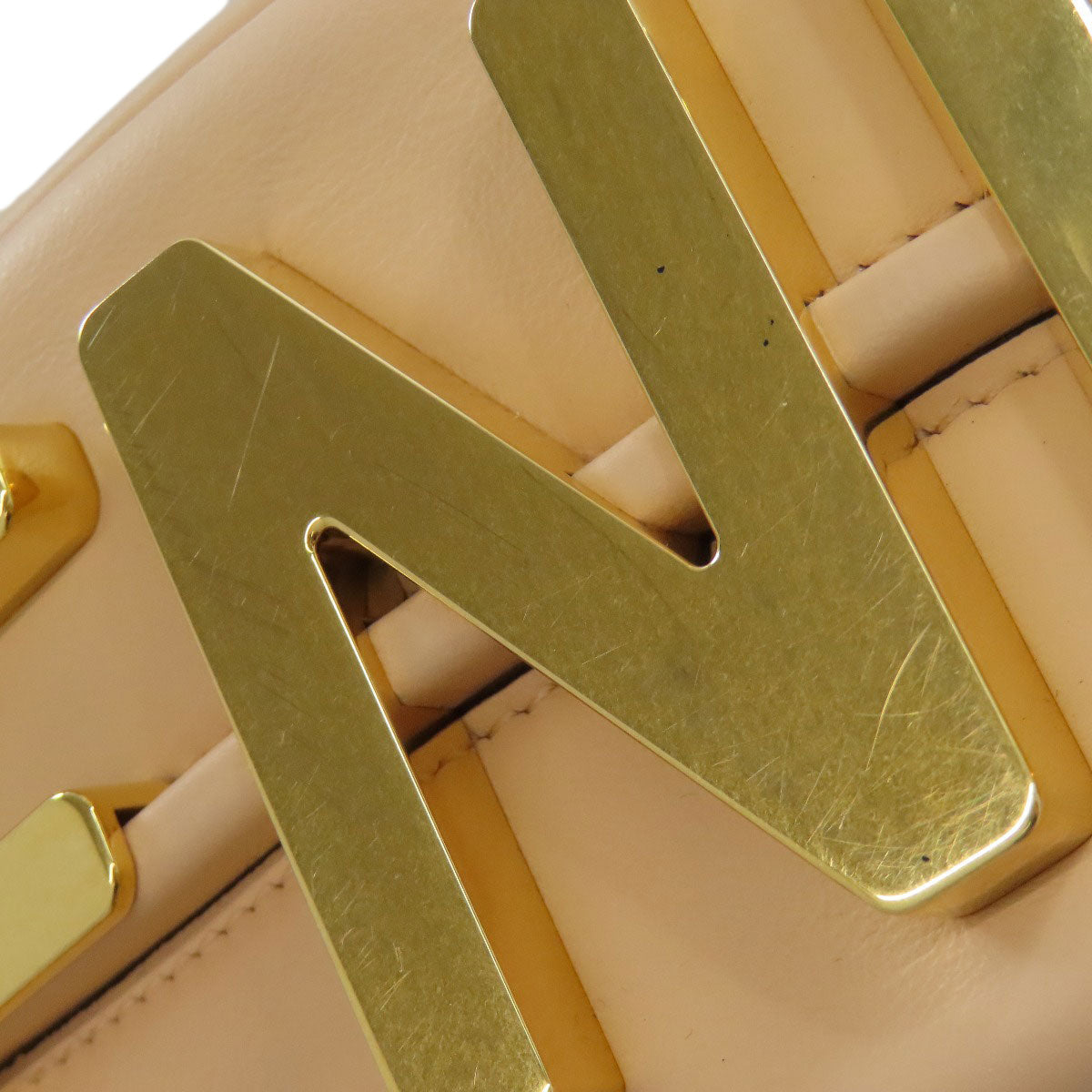 Close-up of a gold belt buckle on a beige leather belt.
