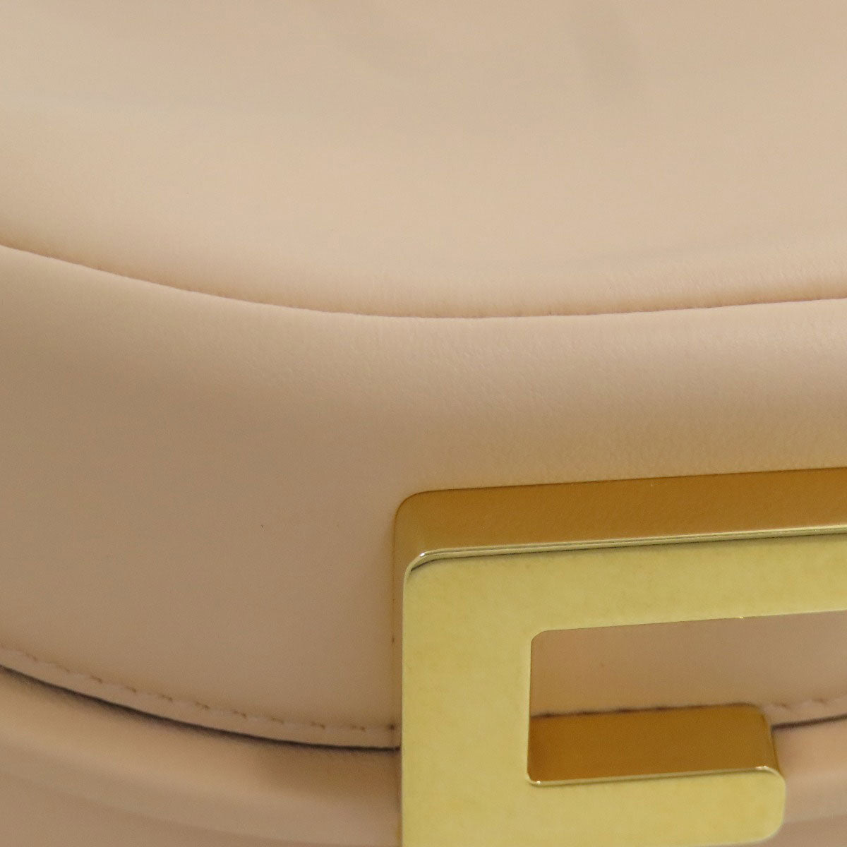 Close-up of a beige handbag with a gold clasp on a light beige background