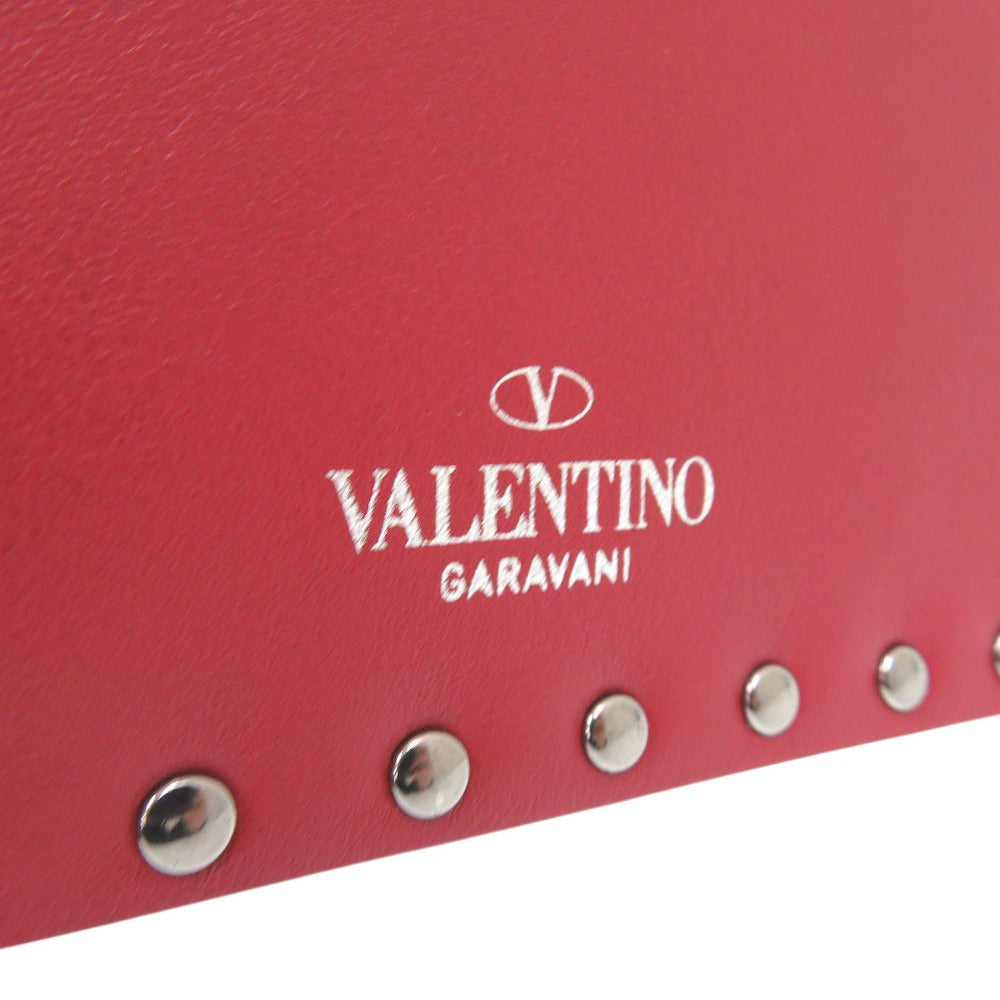 Close-up of a red leather product with 'Valentino Garavani' logo and silver studs.