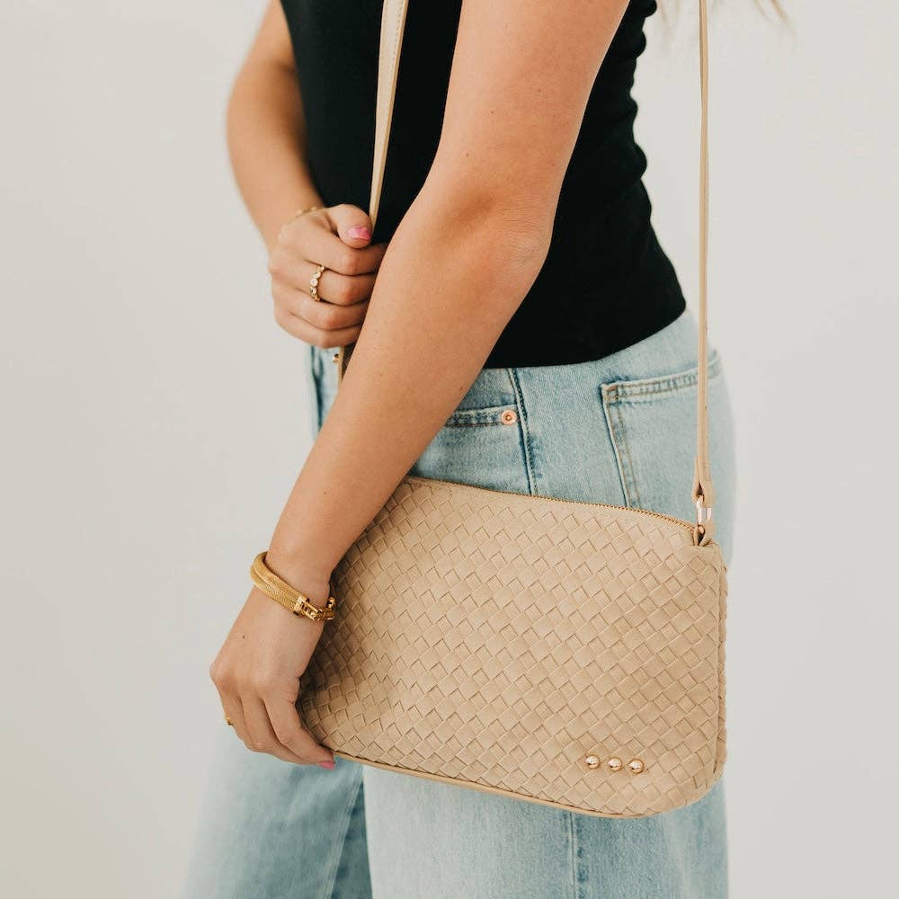 Beige woven handbag held by a person wearing a black top and light blue jeans.