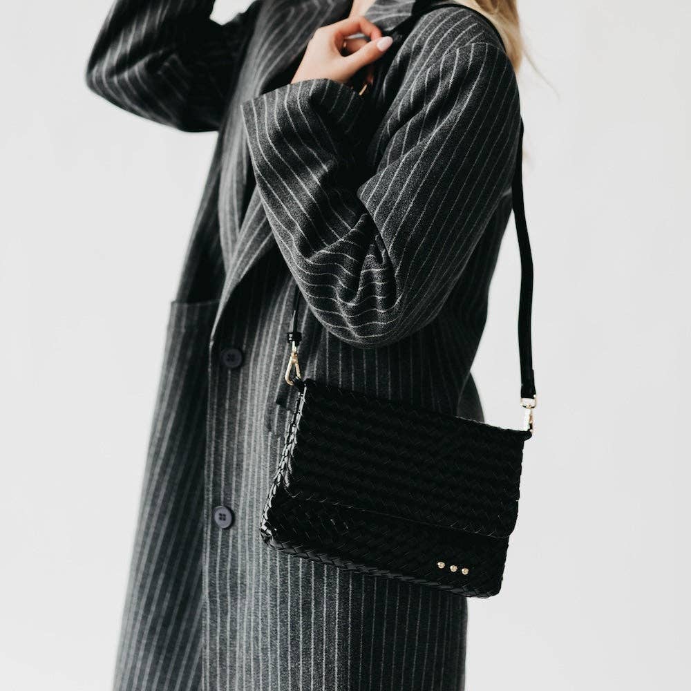 Person wearing a black quilted handbag with a plain background