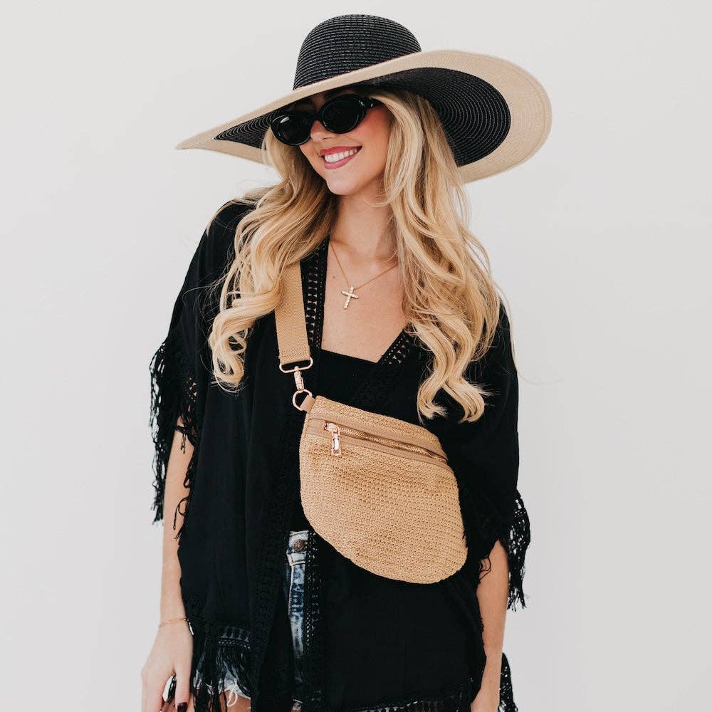 Woman wearing a black sun hat, sunglasses, and a black outfit with a beige handbag on a white background