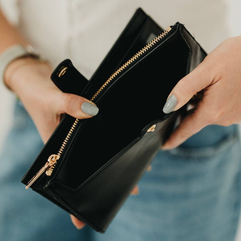 Black clutch with gold zippers held by a person with light blue jeans.