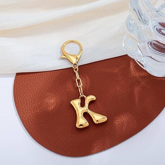Gold keychain with letter 'K' on a brown leather surface